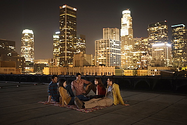A group of friends gathered on a rooftop overlooking a city lit up at night, United States of America