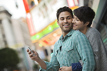 A couple, man and woman hugging on a city street. Man holding a smart phone, United States of America