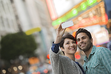 A couple, man and woman on a city street taking a selfy with a smart phone, United States of America