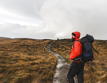 A man in winter clothing, waterproof jacket and rucksack in open countryside by a path, Scotland, United Kingdom