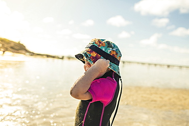 A child in a wetsuit and sunhat on a Cornish beach, England, United Kingdom