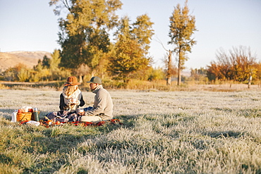 A couple, a man and woman having a winter picnic, sitting on a tartan rug.