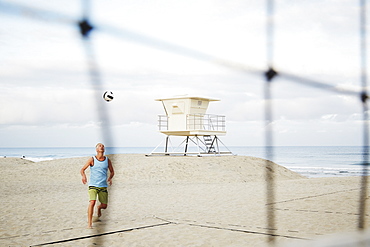 Mature man standing on a beach, playing beach volleyball, United States of America