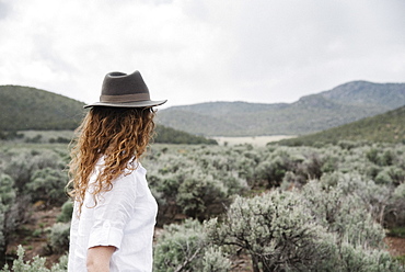 A woman in a fedora standing in an open landscape with a view of mountains woodland and scrub land, United States of America