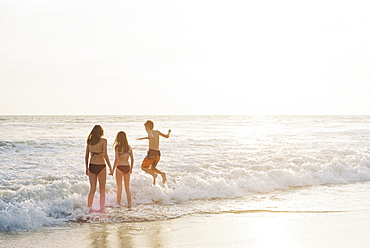 Three children playing on a sandy beach by the ocean.