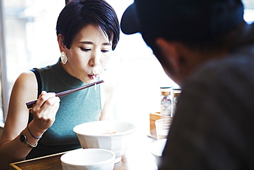 A ramen noodle cafe in a city. A man and woman seated eating noodles from large white bowls, Japan