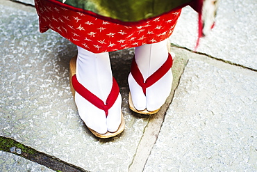 A traditional geisha woman's feet, in wooden soled sandals, with red straps and white stockings or tabi, Japan