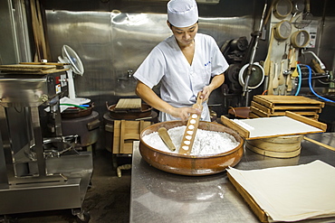 A small artisan producer of wagashi. A man mixing a large bowl of ingredients and pressing the mixed dough into moulds in a commercial kitchen, Japan