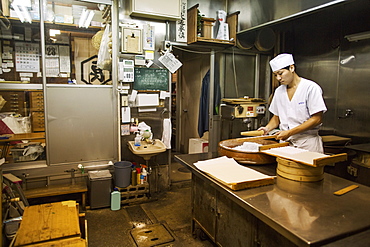 A small artisan producer of wagashi. A man mixing a large bowl of ingredients and pressing the mixed dough into moulds in a commercial kitchen, Japan