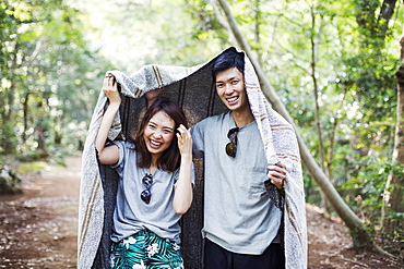 Young woman and man standing in a forest, holding a blanket over their heads, Japan