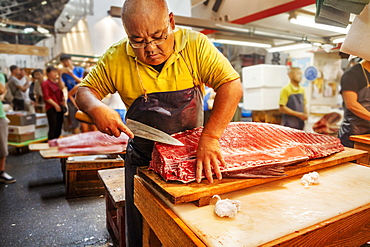 A traditional fresh fish market in Tokyo. A fishmonger working filleting a large fish on a slab. People in the background, Japan