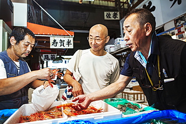 A traditional fresh fish market in Tokyo. Two people selecting shellfish for a customer to buy, filling a bag from boxes of prawns, Japan