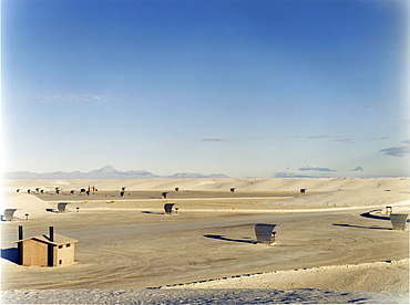 An open space a desert landscape, with a small cabin and sun shelters, surrounded by mountains, USA