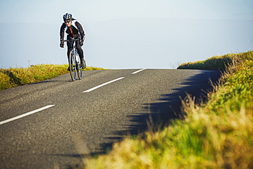 A cyclist riding along a country road on a clear sunny winter day. 