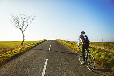 A cyclist riding along a country road on a clear sunny winter day. 