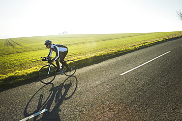 A cyclist riding along a country road on a clear sunny winter day. Shadow on the road surface.