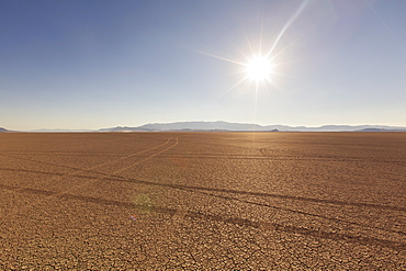 Tyre tracks in a desert landscape with mountains in the distance. against a blue sky.