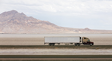 Lorry driving on a road through a desert landscape with mountains in the background.