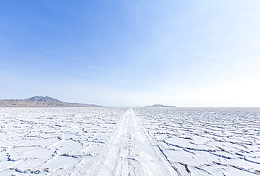 Cracked earth in a desert landscape against a blue sky with mountains in the distance.