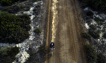 High angle view of man riding cafe racer motorcycle along dusty dirt road, United States of America