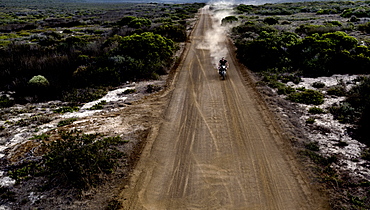 Landscape with man riding cafe racer motorcycle along dusty dirt road, United States of America