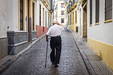 Rear view of elderly man with cane walking along cobbled street in Sevilla, Andalusia, Spain, Seville, Andalusia, Spain