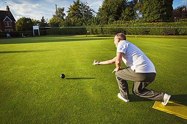 A lawn bowls player standing on a small yellow mat preparing to deliver a bowl down the green, the smooth grass playing surface, England, United Kingdom