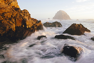 Seascape with breaking waves over rocks at dusk.