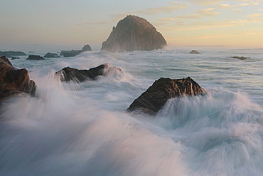 Seascape with breaking waves over rocks at dusk.