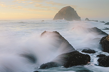 Seascape with breaking waves over rocks at dusk.