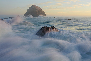 Seascape with breaking waves over rocks at dusk.