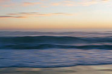 Seascape with breaking waves under cloudy sky at sunset.