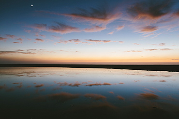 Seascape with dramatic sky reflected in water at dusk.