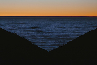 Seascape with ocean at dusk, hills in foreground.