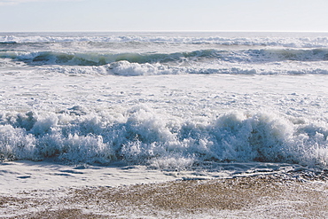 Seascape with breaking waves on sandy beach.