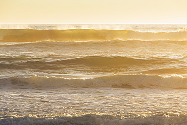 Seascape with breaking waves under cloudy sky at sunset.