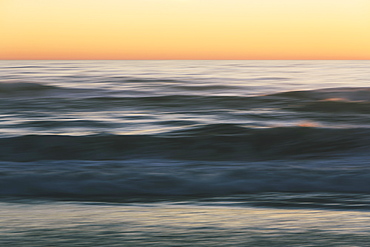 Seascape with breaking waves under cloudy sky at sunset.