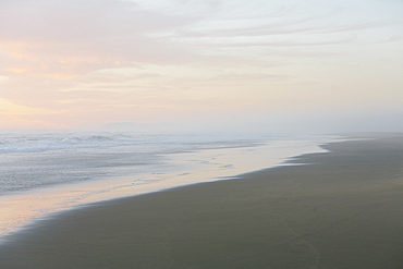 Landscape with sandy beach and ocean at sunset.