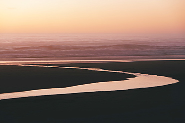 Landscape with small stream flowing into surf at dusk.