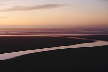 Landscape with small stream flowing into surf at dusk.