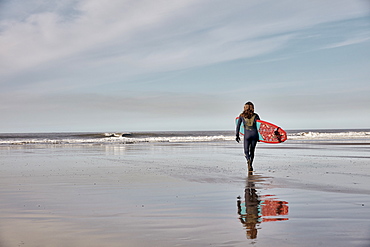 Man holding a surf board walking out to the sea at low tide, United Kingdom