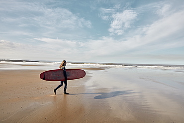 Man in a wetsuit walking towards sea holding a surf board, United Kingdom