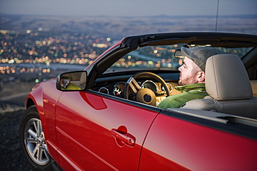 A Caucasian male parked in his convertible sports car watching the sunset over the Clearwater River and the city of Lewiston Idaho, United States of America