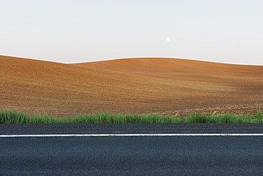 Moonrise over rolling freshly planted fields, road in foreground, Washington, United States of America