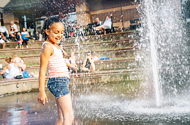 Smiling girl playing in public fountain in summer, United States of America