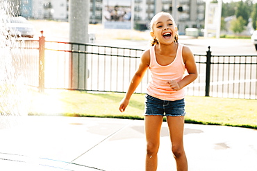 Smiling girl playing in public fountain in summer, United States of America