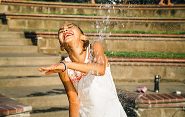 Smiling girl playing in public fountain in summer, United States of America