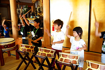 Group of pre-school children playing the drums in a Japanese temple, a traditional religious practise, Kyushu, Japan