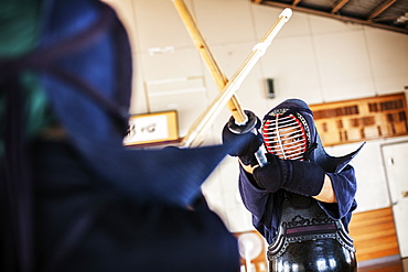 Two Japanese Kendo fighters wearing Kendo masks practicing with wood sword in gym, Kyushu, Japan