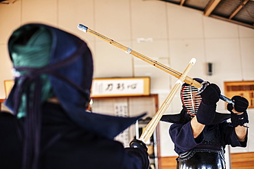 Two Japanese Kendo fighters wearing Kendo masks practicing with wood sword in gym, Kyushu, Japan